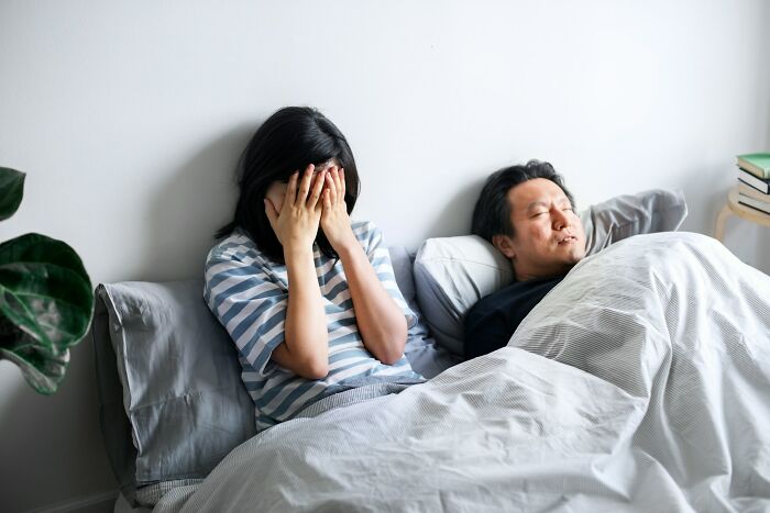 Stressed woman covering her face while man sleeps beside her, illustrating relationship advice for couples dealing with conflict.