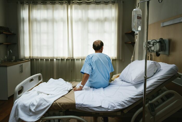 Man in hospital gown sitting on bed in hospital room, reflecting on changes in spouse after wedding and ignored red flags.