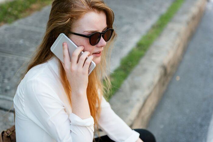 Young woman with sunglasses sitting outdoors on steps, talking on phone, reflecting on chaotic breakup stories.