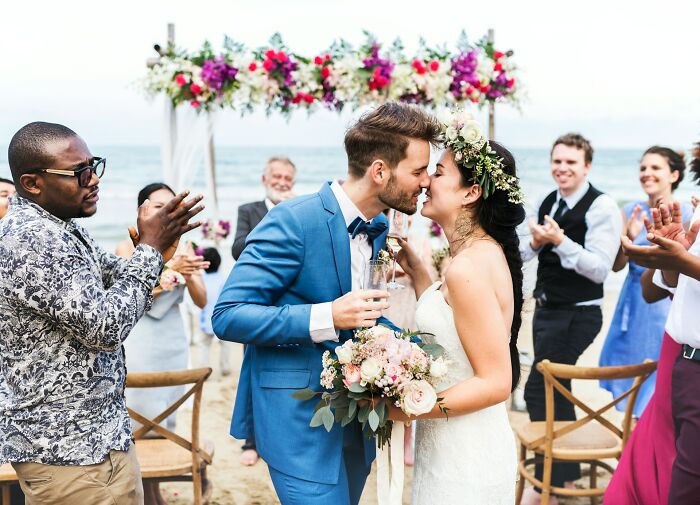 Couple kissing at a beach wedding with guests clapping, capturing chaotic breakup stories that sound straight out of a movie.