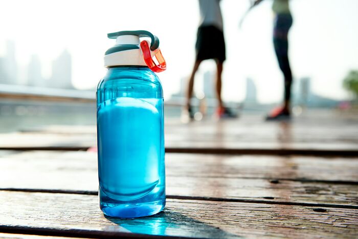 Blue water bottle on wooden deck with two blurred people in background.