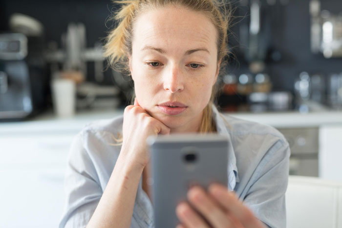 Woman with concerned expression looking at smartphone focusing on mom whitewashing biracial daughter's curls debate online.