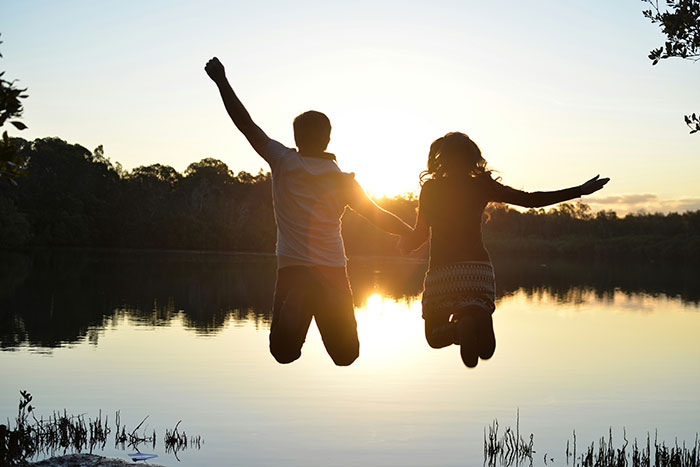 Silhouetted couple holding hands and jumping by a lakeside at sunset, symbolizing rejection and new dating after bestie drama.