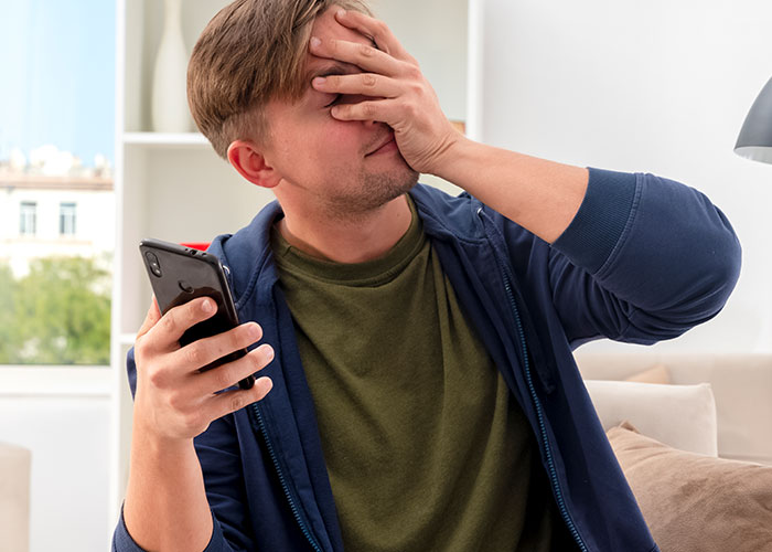 Dad upset about daughter&rsquo;s home, holding phone and covering face with hand, showing worry and frustration indoors.