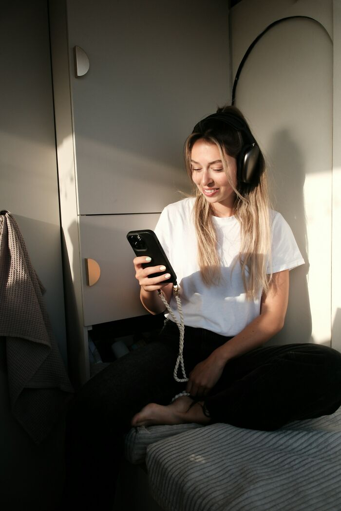 Young woman wearing headphones, smiling while looking at phone, illustrating signs someone is having an affair.