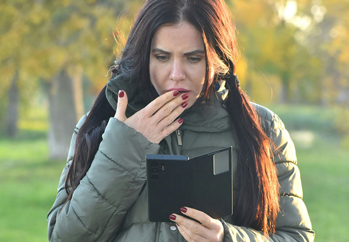 Woman in a green jacket looking shocked at her phone, capturing emotions related to rejection and dating after heartbreak.