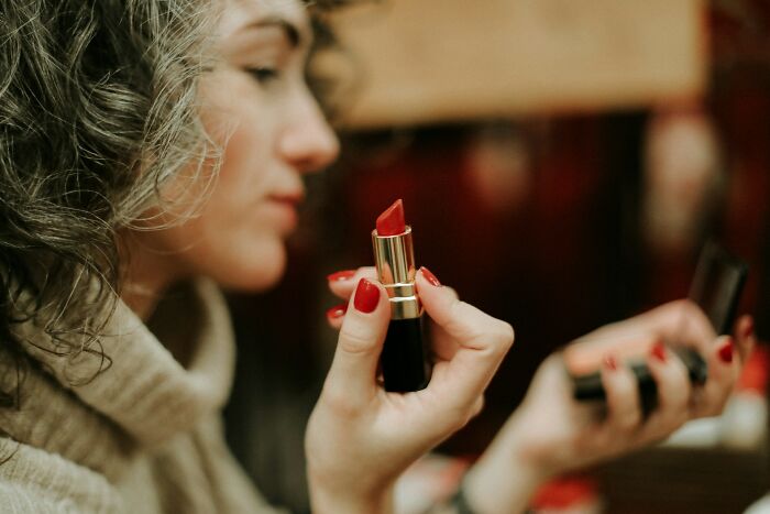 Woman with curly hair holding red lipstick and compact mirror, related to wedding guests making bride and groom regret.