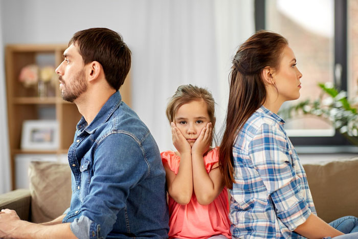 Frustrated couple sitting back to back with unhappy child between them, illustrating conflicts dating men with kids.