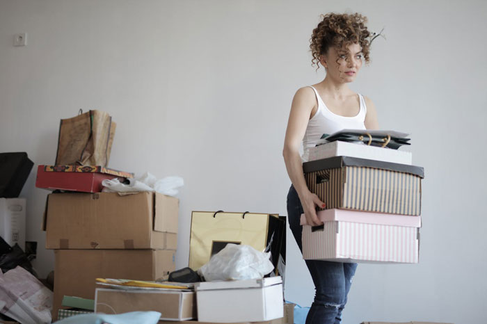Young woman carrying stacked boxes in a room, symbolizing parents kick out daughter so they move into her remodeled space.