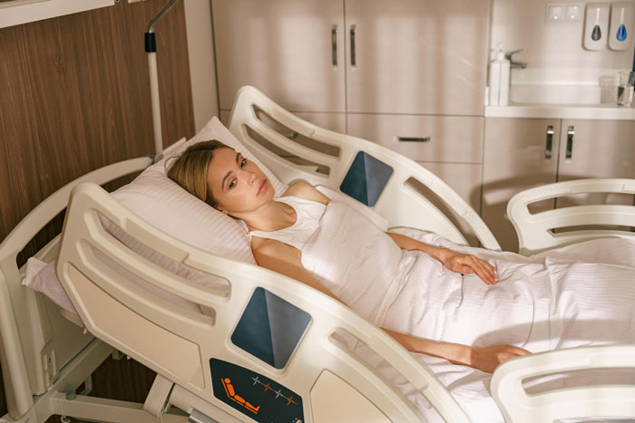 Woman lying in a hospital bed looking concerned while waiting during a family emergency with a boy&rsquo;s trip affair disguise.