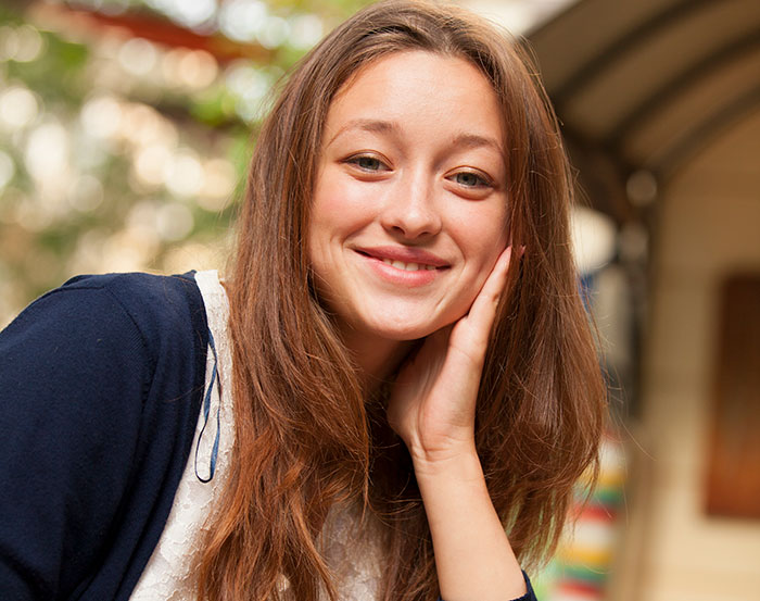 Young woman smiling thoughtfully, representing sibling refusing to keep paying rent to parents after sister lives rent free