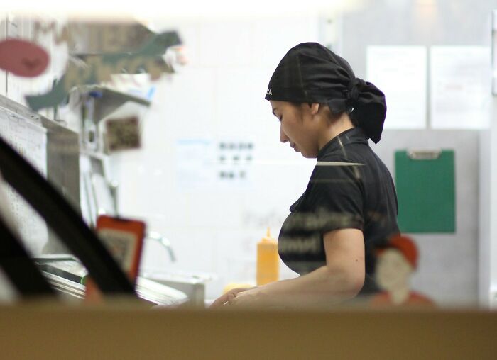 Woman in black uniform and headscarf working in a restaurant kitchen, illustrating cheating signs in women concept.