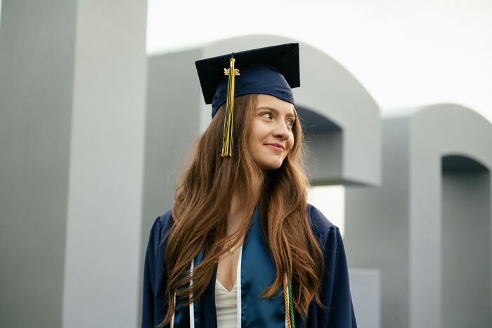 Young woman in graduation cap and gown looking aside, symbolizing personal growth and long grudges held over time.