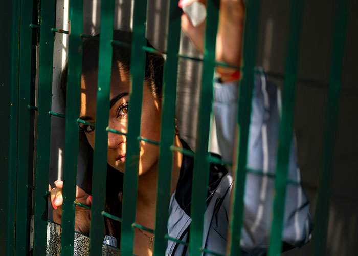 Young woman behind green metal bars, symbolizing the villain in someone else’s story and impacting lives profoundly.