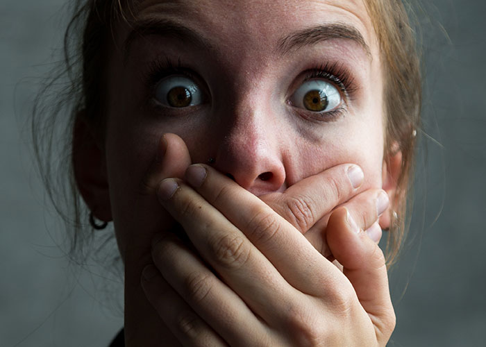 Woman with wide eyes covering her mouth in shock, illustrating the concept of being a villain in someone else’s story.