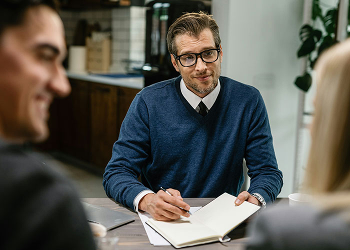 Man in glasses and blue sweater taking notes during a serious discussion about villains in someone else’s story.