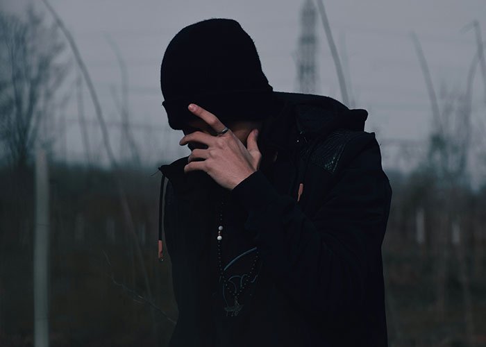 Person in dark clothing and a beanie covering their face outdoors, representing a villain in someone's story.