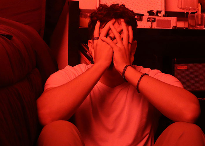 Young man covering his face with hands, sitting on the floor, illustrating stress and villain perspective in personal stories.