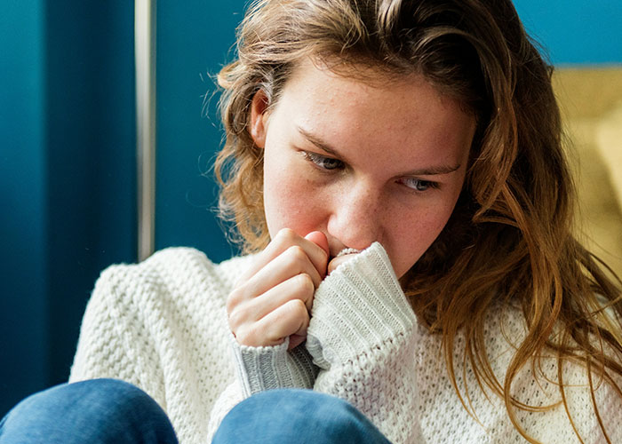 Young woman in a white sweater looking anxious and pensive, reflecting on being a villain in someone else’s story.