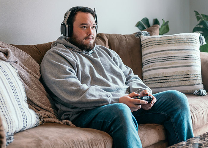 Man wearing headphones and playing video games on a couch, representing villain in someone else’s story concept.