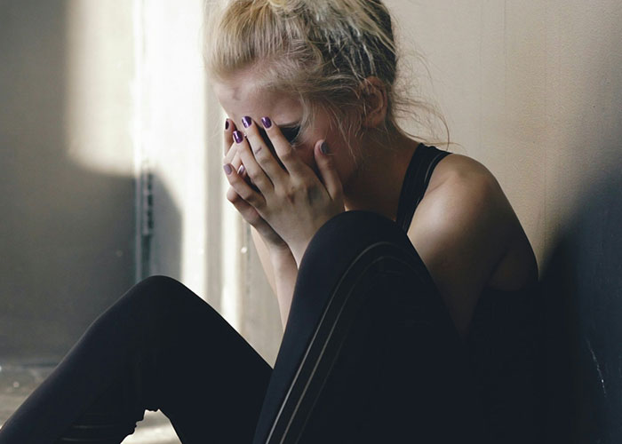 Young woman sitting on the floor with her face in her hands, conveying distress and destruction of lives theme.