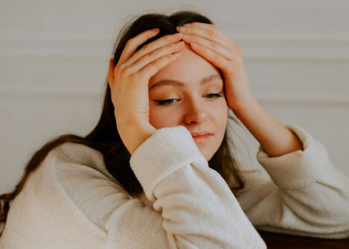 Young woman in a white sweater holding her head, expressing stress and reflecting on being a villain in someone else’s story.