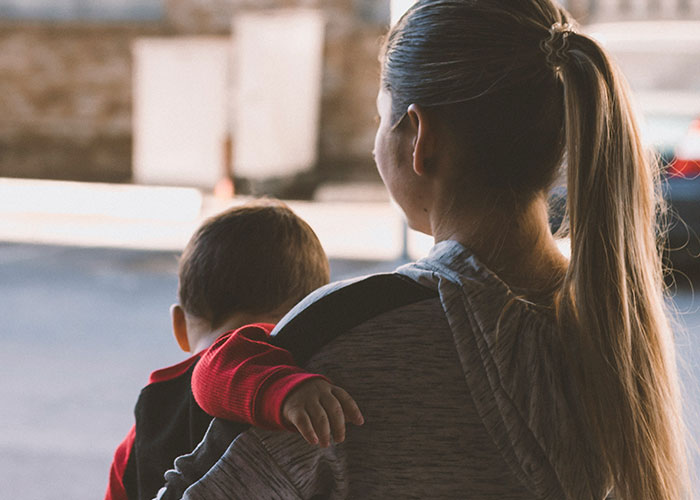 Woman with a ponytail carrying a child in a red sweater, symbolizing perspectives of villains in someone else’s story.