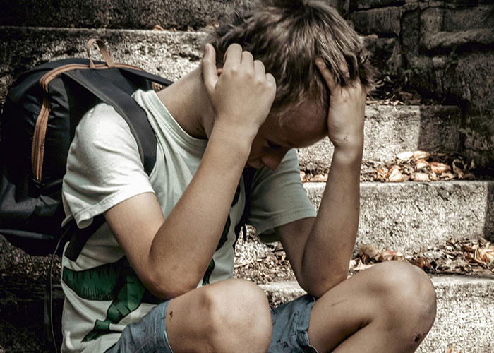 Young boy sitting on stone steps holding his head in distress, illustrating the impact of villain actions in people's lives.