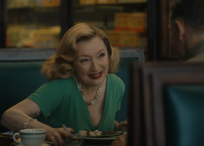 Woman in a green dress smiling and talking while sitting in a diner booth in Netflix's Monster The Ed Gein Story.