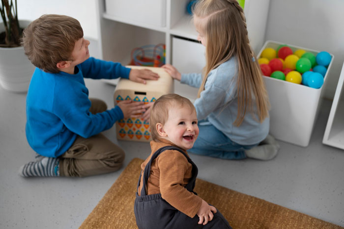 Three young children playing together on the floor in a home environment with colorful toys around them