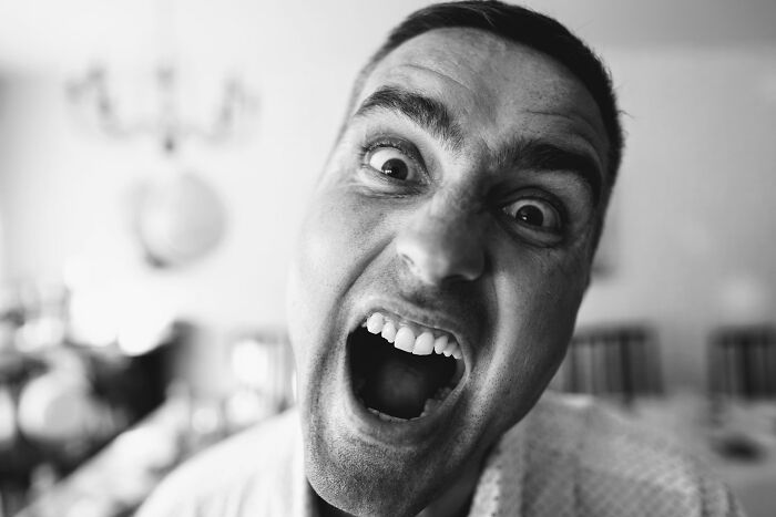 Close-up black and white photo of a man making an exaggerated face, capturing a chaotic wedding guest moment.