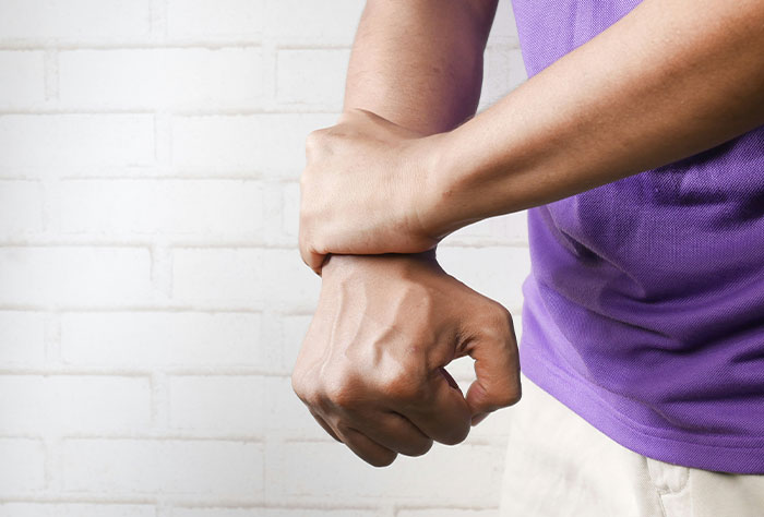 Person in purple shirt holding wrist, illustrating pain or symptoms related to Google diagnosing people.