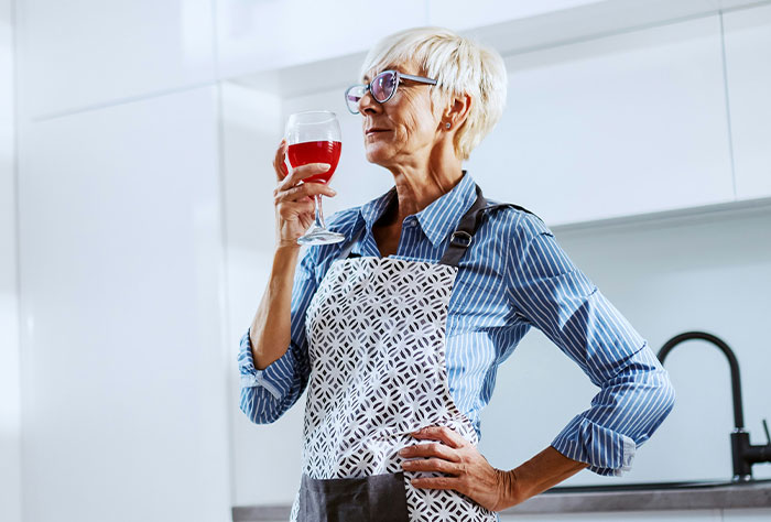 Mature woman in apron holding a glass of wine in kitchen illustrating Google diagnosing people accuracy.
