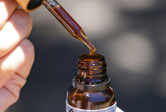 Close-up of a hand holding a dropper above a brown bottle, illustrating accurate medical diagnosis concepts.