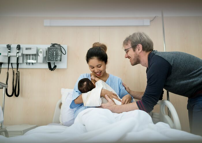 New parents smiling and bonding with their newborn baby in a hospital setting after birth.