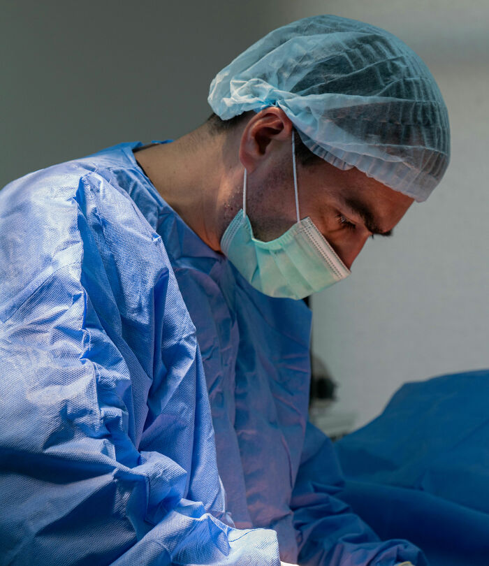 Surgeon in blue scrubs and mask focused during a birth procedure, capturing craziest and funniest moments at delivery.