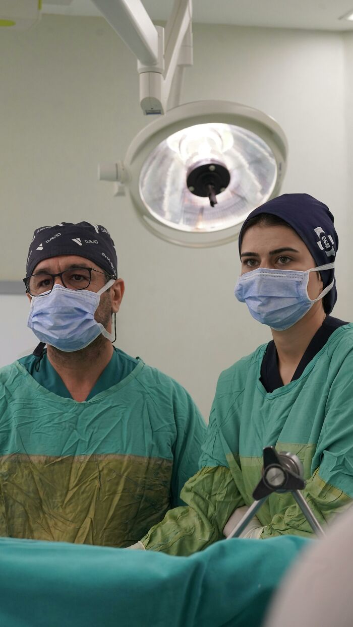 Two surgeons wearing masks and scrubs focused during birth in an operating room under surgical light.