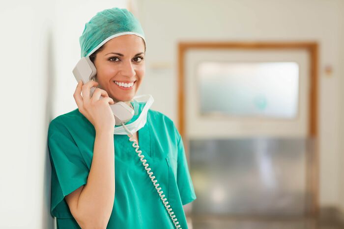 Female doctor in green scrubs smiling and talking on a phone, representing craziest and funniest things during birth.