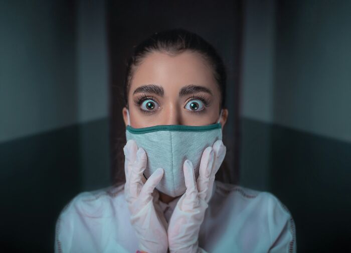 Hospital worker wearing a mask and gloves with wide eyes, expressing fear while sharing creepy experiences at work.