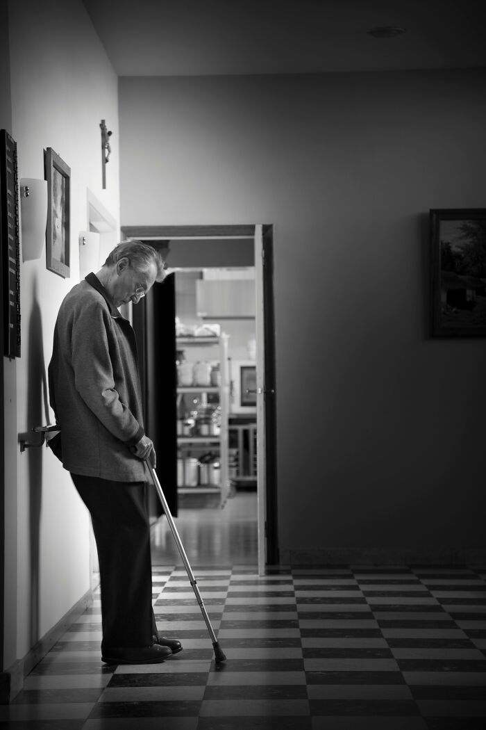 Elderly man with cane standing alone in a dimly lit hospital hallway, evoking a creepy hospital worker experience.