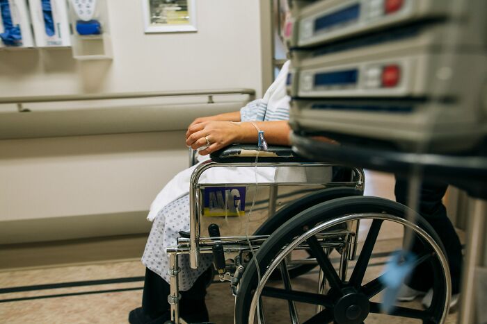 Patient in wheelchair with IV drip in hospital hallway, reflecting hospital workers creepy experiences while working.