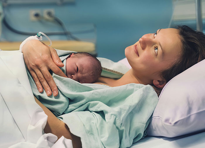 Mujer en sala de partos sosteniendo a recién nacido, representación del caos en salas de parto tras descubrir infidelidad.
