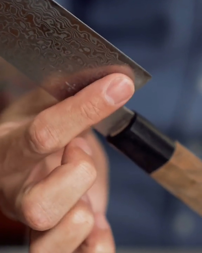 Close-up of a hand holding a patterned knife blade, highlighting a common mistake causing avocado hands injuries.