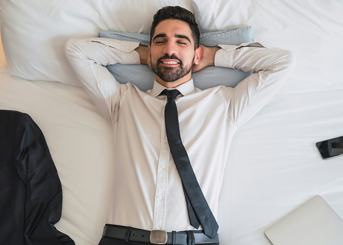 Man in dress shirt and tie lying on bed with eyes closed, reflecting on benefits of women getting married.