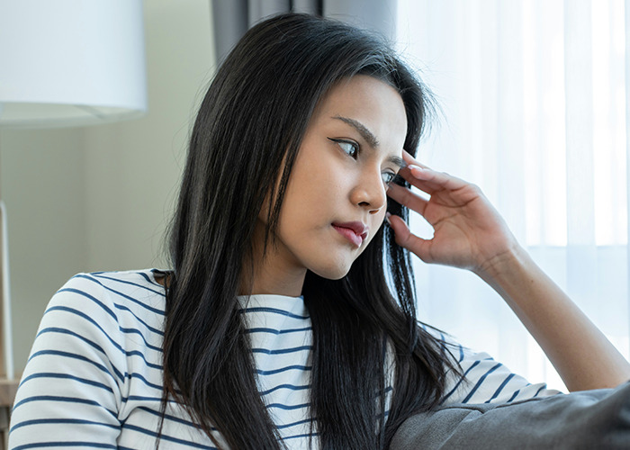 Woman in striped shirt sitting indoors, looking thoughtful while contemplating the benefits of marriage for women.
