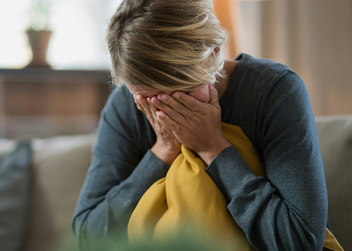 Woman sitting on couch covering her face with hands, reflecting on the real benefit of marriage for women.