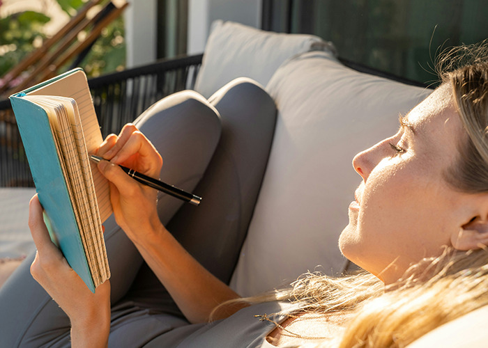 Woman relaxing outdoors in sunlight, writing in a notebook, reflecting on benefits of marriage for women.