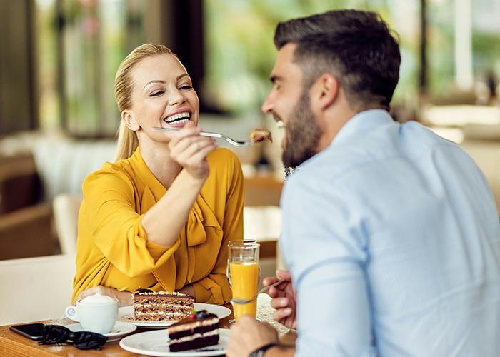 Woman playfully feeding partner dessert during a date, illustrating benefits of marriage for women in a casual restaurant setting.