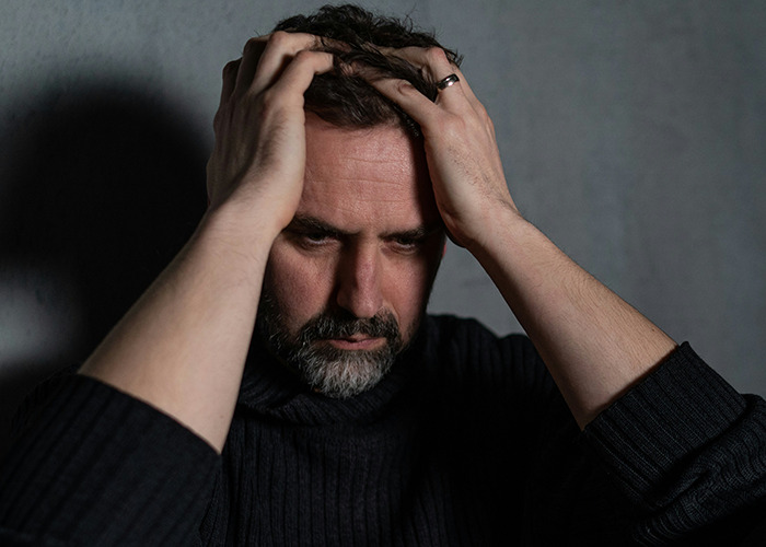 Man with beard holding his head in frustration, reflecting on benefits of marriage for women, in a dimly lit room.