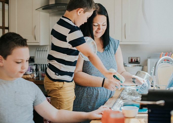 Woman and children washing dishes together in kitchen, illustrating the benefits of marriage for women and family life.